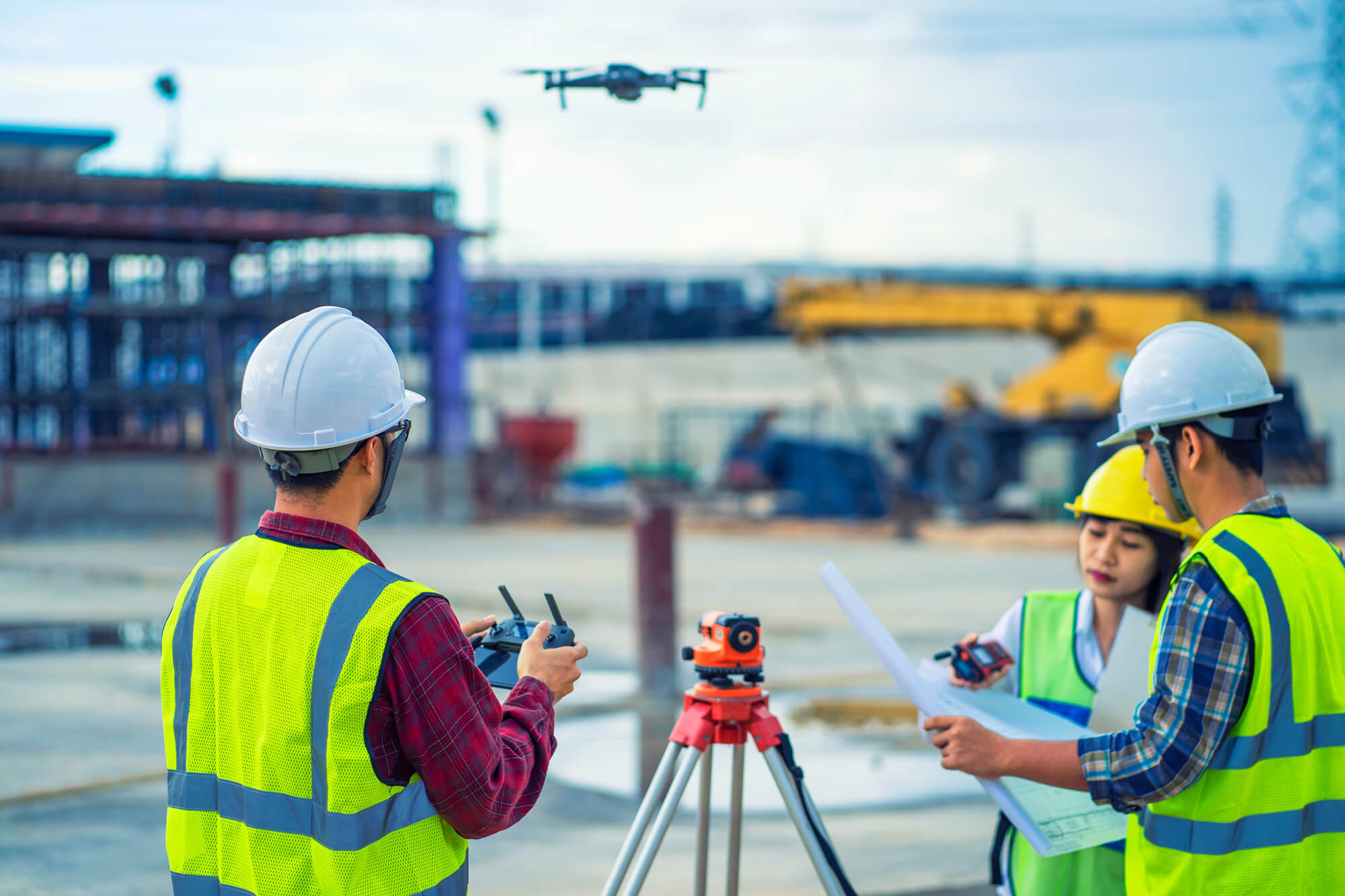 Des ouvriers du bâtiment portant des gilets de sécurité et des casques utilisent un drone et examinent les plans sur un chantier actif.